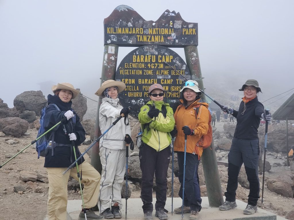 Five trekkers at foggy barafu camp sign on Mount Kilimanjaro