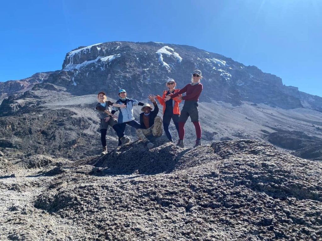 Five trekkers standing on lava rock below the summit dome of Kilimanjaro