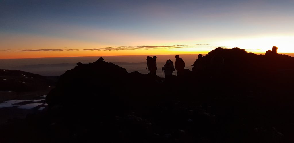 Four trekkers silhouetted against the sunrise above a layer of cloud on Kilimanjaro