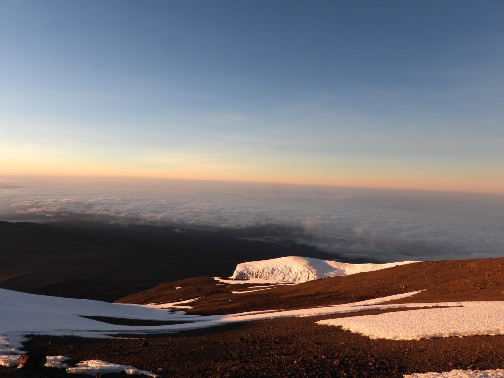 Glacier cliff and fresh snow patches above a cloud sea at sunrise on Mount Kilimanjaro