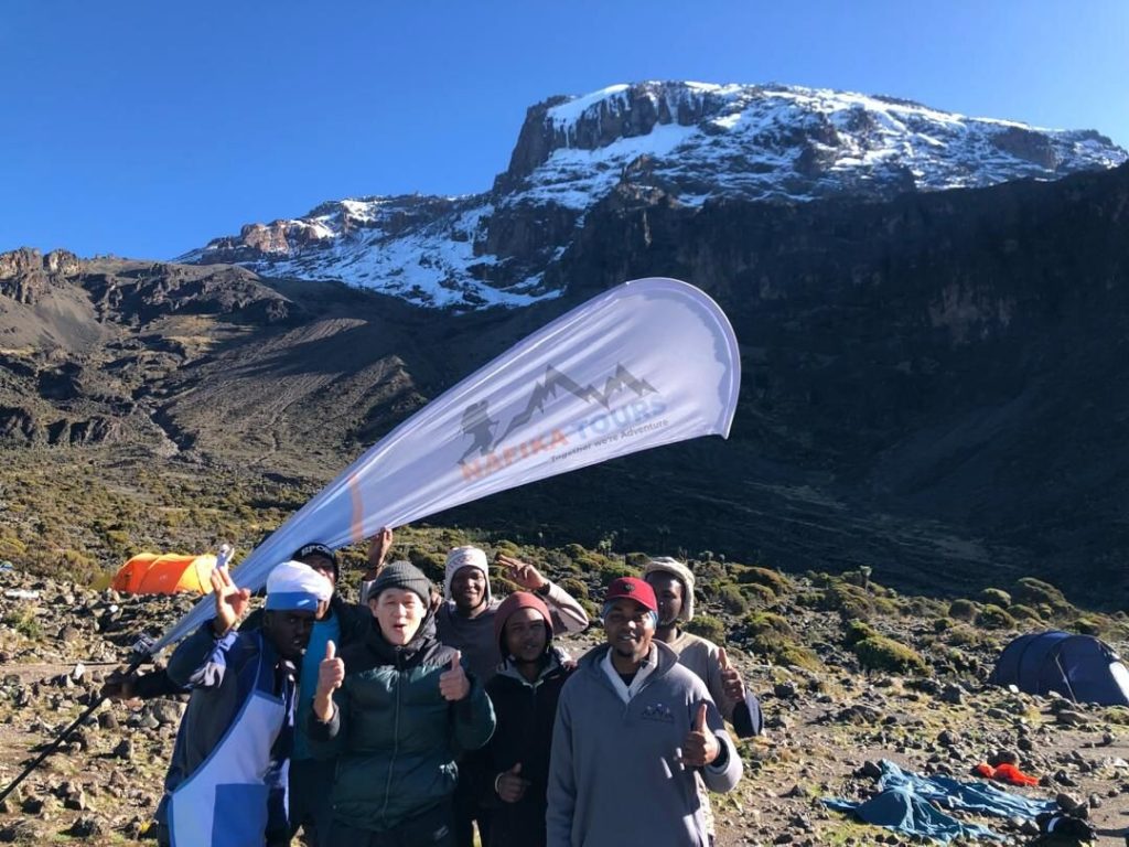 Trekking group holding an operator banner below the snowy cliffs of Kilimanjaro
