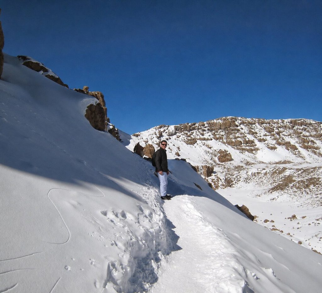Trekker in softshell trousers and a light jacket on a snowy rocky slope on Mount Kilimanjaro
