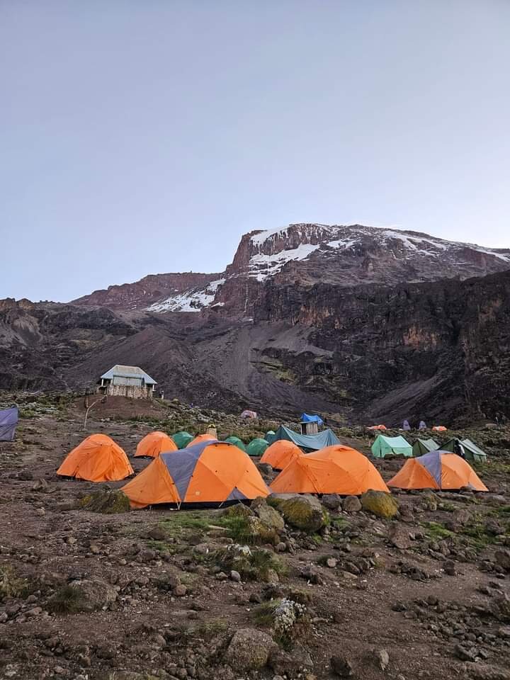 Orange tents at a high camp below a snowy cliff at dusk on Mount Kilimanjaro