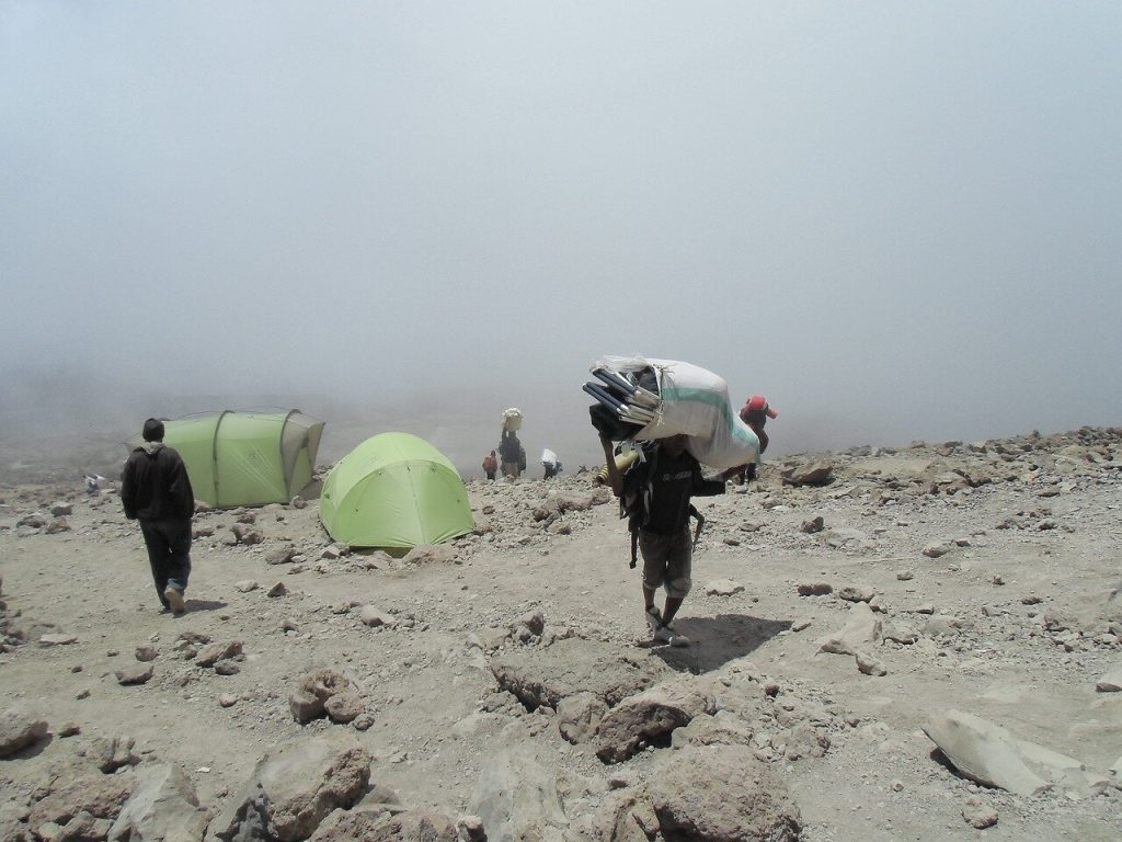 Porter carrying a load through a misty alpine desert camp on Mount Kilimanjaro