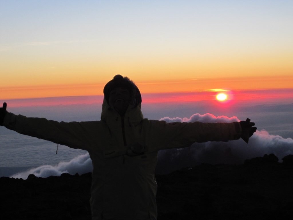 Trekker silhouetted with arms outstretched at sunrise on the summit of Mount Kilimanjaro