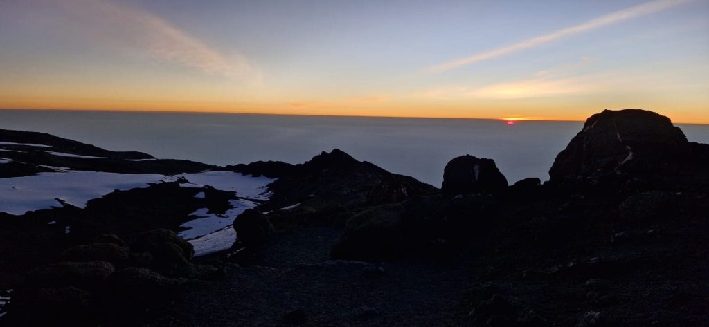 Sunrise above the clouds seen from snowy summit rocks on Mount Kilimanjaro