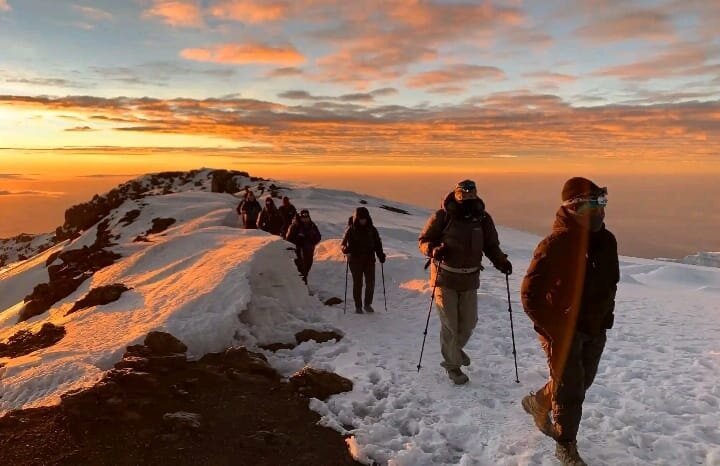 Trekkers on snowy summit ridge at sunrise on Mount Kilimanjaro
