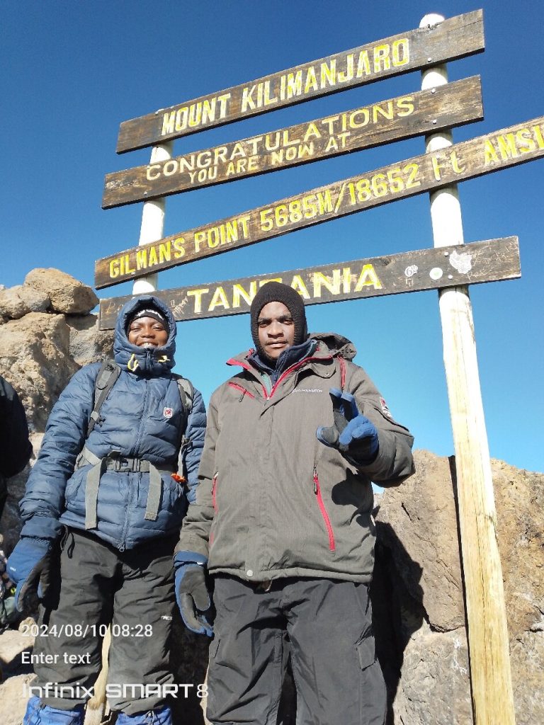 Two climbers at the Gilman’s Point signboard, the crater rim reached from the Marangu Route
