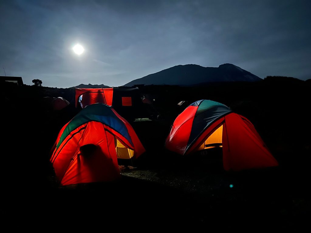 Two glowing red tents under moonlight on Mount Kilimanjaro