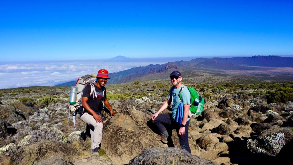 Two trekkers on moorland boulders above the cloud layer, typical of the quiet Lemosho approach