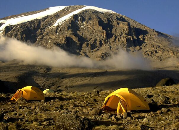Two yellow tents below snowcapped summit dome on Mount Kilimanjaro